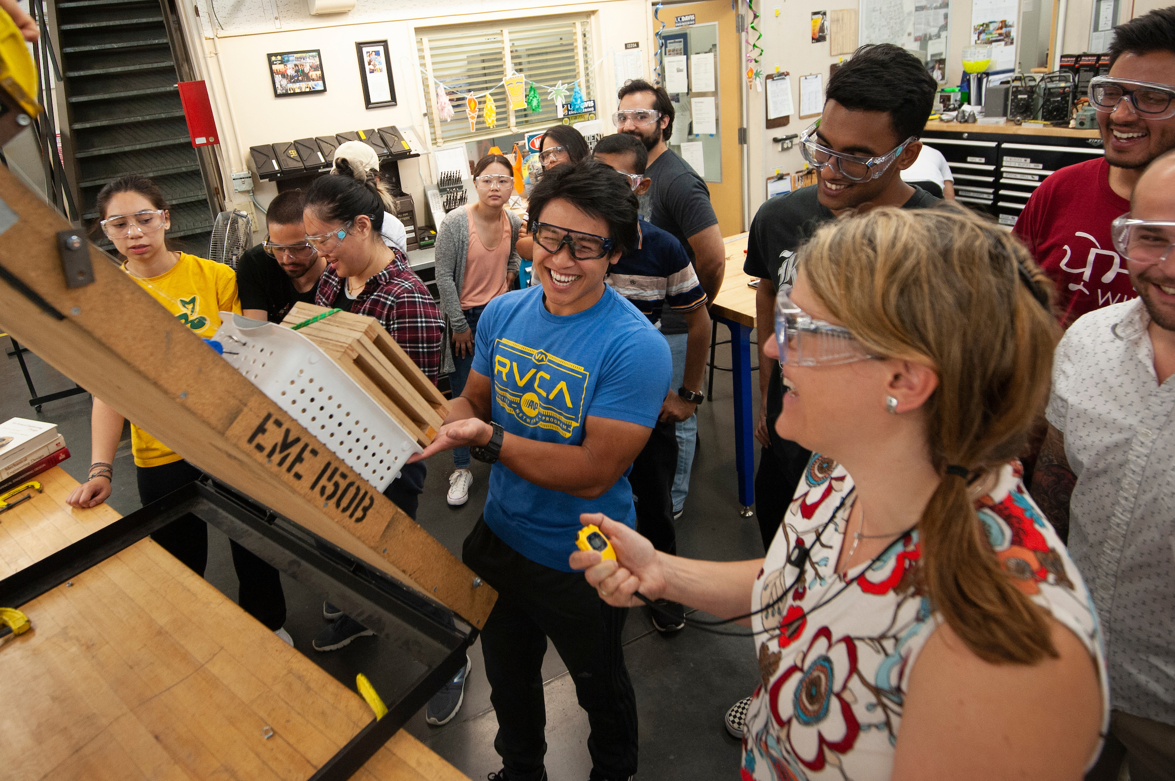 A group of students wearing safety goggles smile and laugh while compete in an engineering contest. 