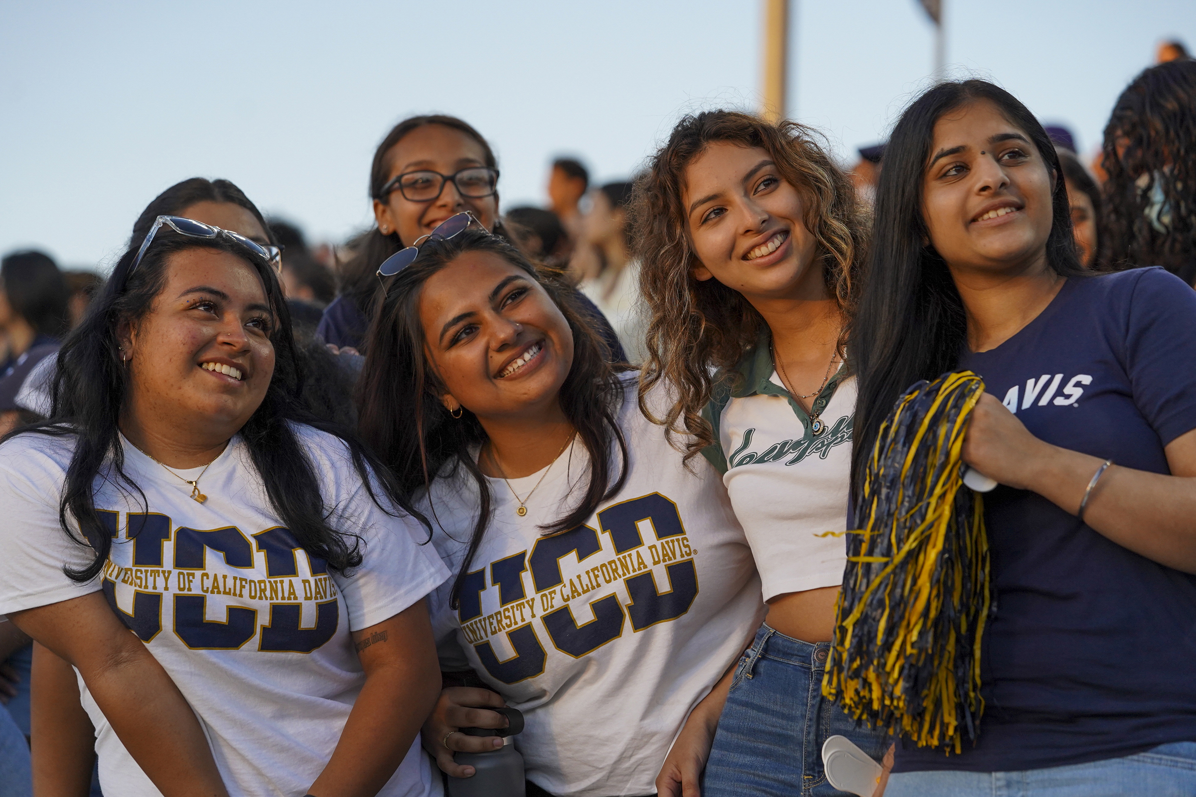 A group of students wearing UC Davis apparel smile as they pose for a photo in UC Davis Health stadium.