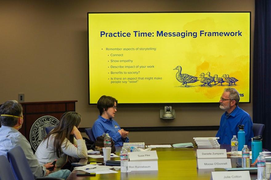 three people at a table talking with a presentation in the background