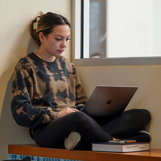 Student sitting in a nook, typing on a laptop